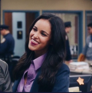 Latina in a blue suit with purple shirt smiling. Her name is Amy Santiago